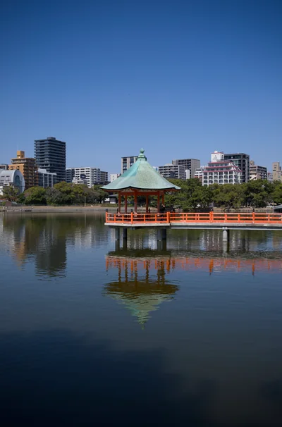 An orange lakeside pavilion and its reflection beneath a clear blue sky