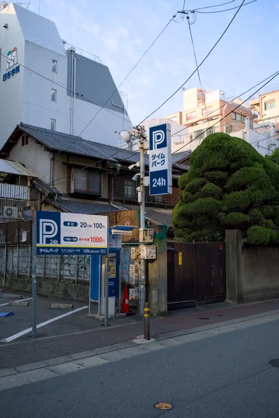 A quiet Japanese street with parking signs, overhead wires and a sculpted tree