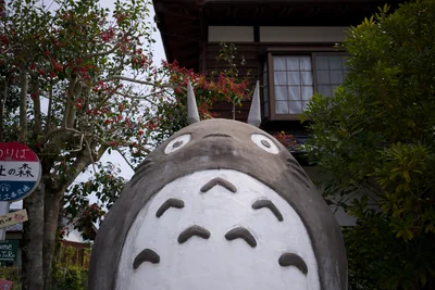 A large Totoro figure outside a wooden building, surrounded by foliage
