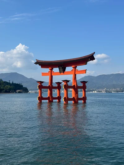 A vermilion torii gate standing in blue water with mountains beyond