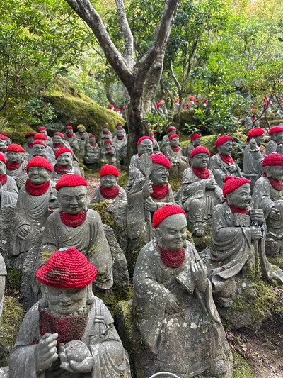 Stone statues wearing red knitted hats among moss and trees