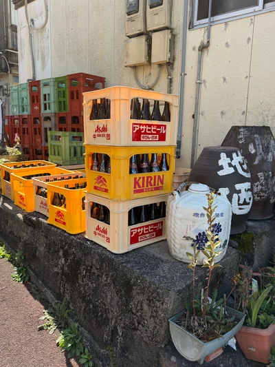 Sunlit stacks of yellow and cream beer crates beside ceramic sake jars